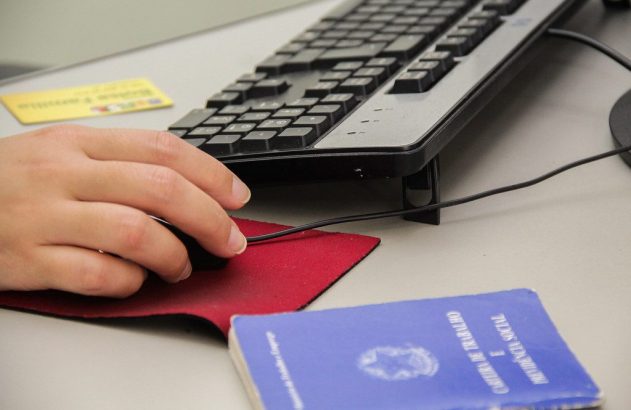 Mão opera mouse do computador. Teclado, carteira de trabalho e cartão sobre a mesa.