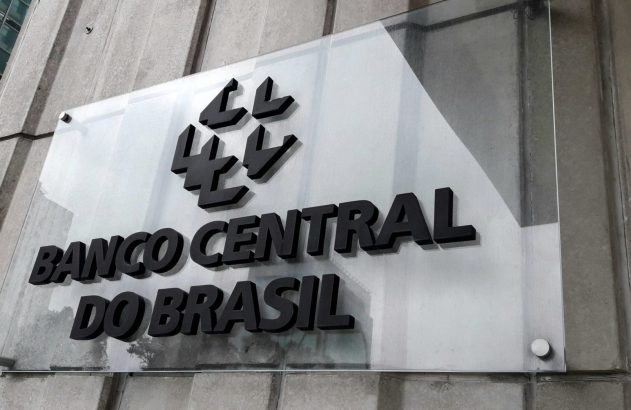 Placa do Banco Central do Brasil em painel transparente com logotipo, na fachada de edifício.