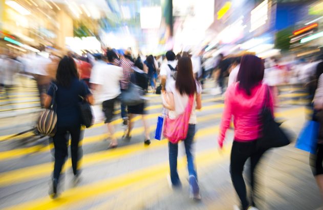Multidão de pessoas em movimento rápido atravessando faixa de pedestres em rua movimentada da cidade.