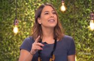 Mulher sorri e gesticula, com fundo de folhagem verde e lâmpadas acesas.