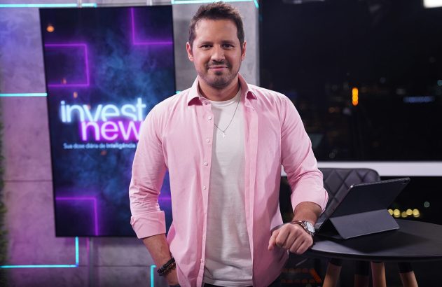 Apresentador de camisa rosa em estúdio do InvestNews, em pé e olhando para a câmera.