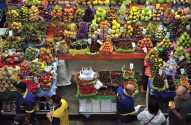 Vista aérea de um mercado de frutas com barracas repletas de pilhas coloridas de frutas e pessoas.