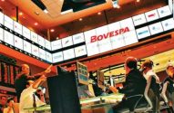 Corretores negociam ativamente em pregão da bolsa BOVESPA, com telas e painéis de dados ao fundo.