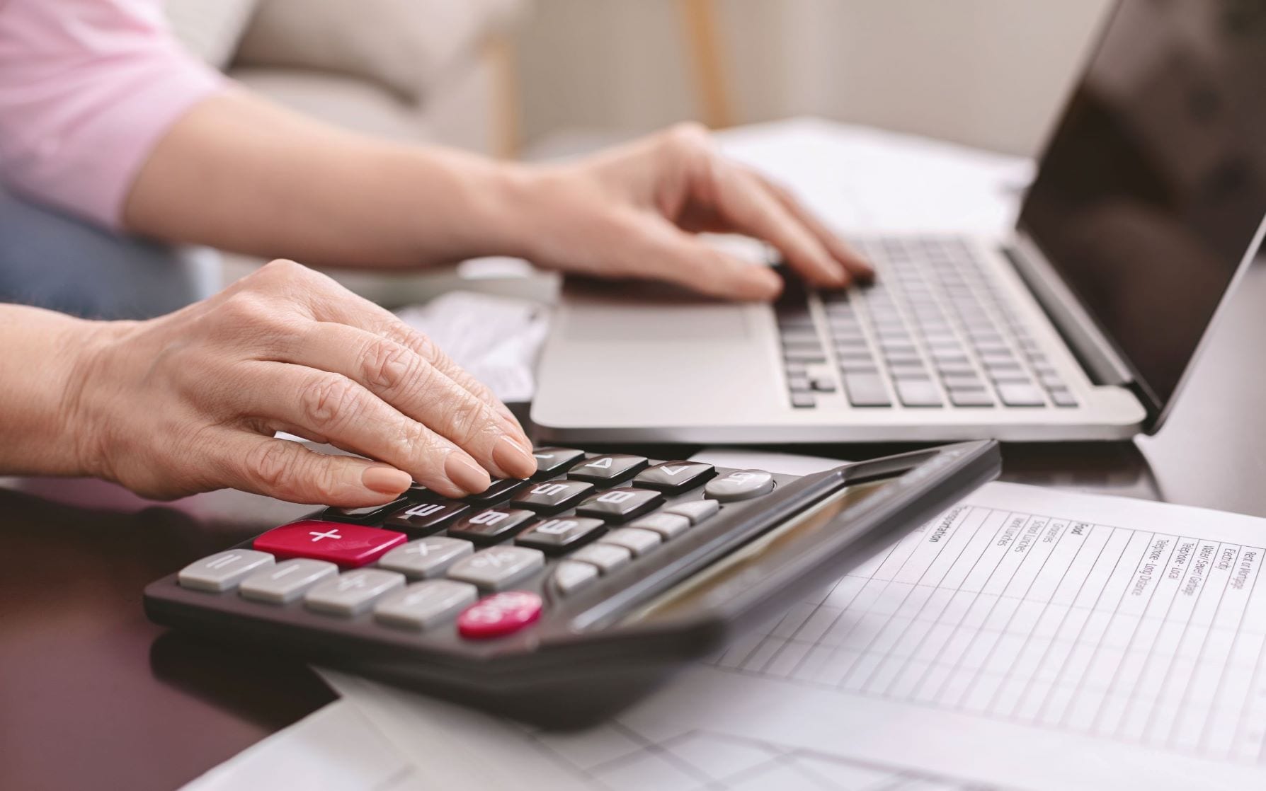 Mulher fazendo conta com calculadora e notebook, simulando a criação do IR