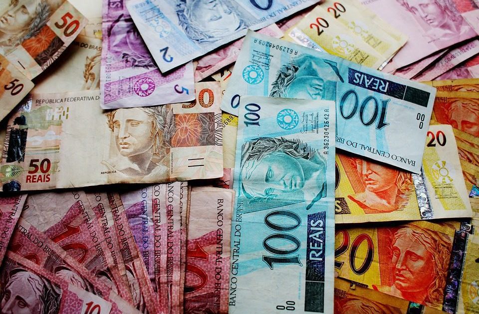 Uma pilha de notas de Reais brasileiros coloridas, de diferentes valores, como 10, 20, 50 e 100 Reais.