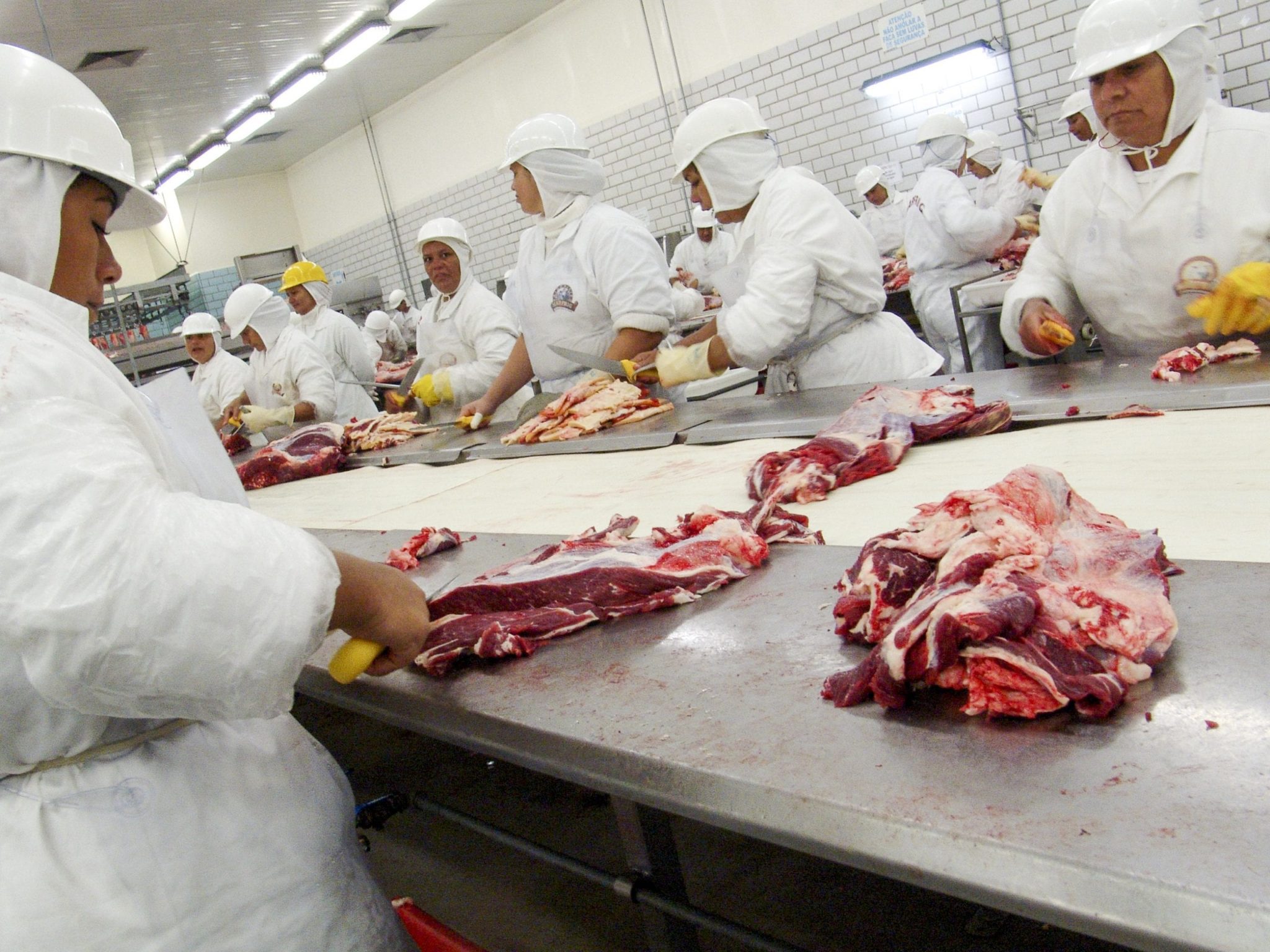 Frigorífico e pessoas cortando carne