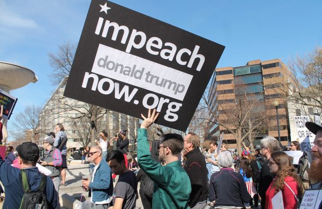Pessoa segura cartaz preto: 'impeach donald trump now.org' com estrela, em protesto.