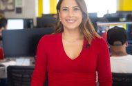Mulher de blusa vermelha com microfone de lapela sorri em escritório.