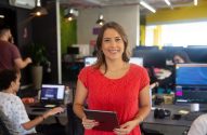 Mulher de vermelho sorrindo com tablet no escritório.