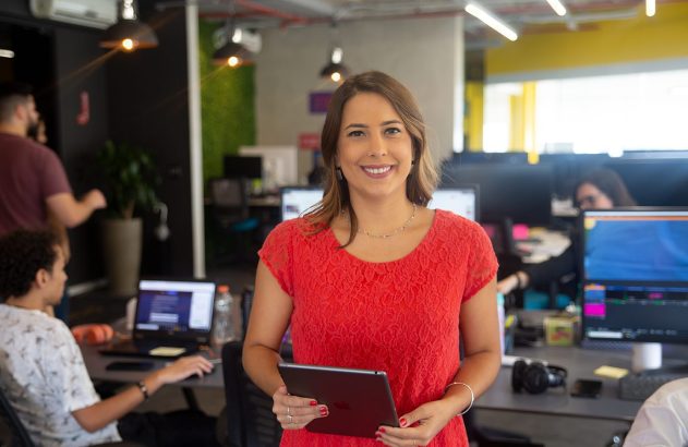 Mulher de vermelho sorrindo com tablet no escritório.