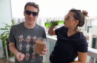 Homem segura pote de amendoins e mulher bebe garrafa em sacada.