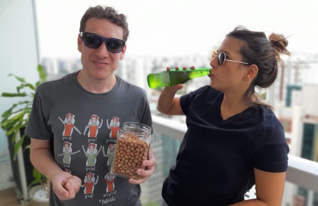 Homem segura pote de amendoins e mulher bebe garrafa em sacada.