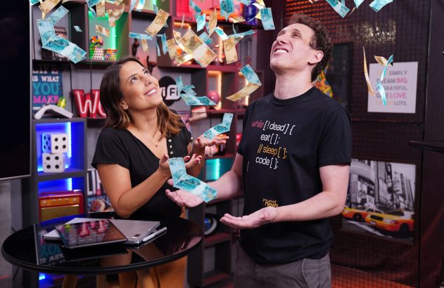 Homem e mulher sorrindo e olhando para cima enquanto notas de Real caem sobre eles.