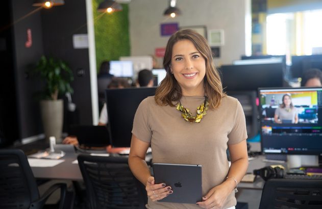 Profissional sorridente em escritório moderno, segurando tablet e olhando para a câmera.