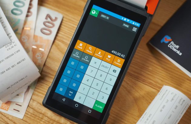 Terminal POS com tela de calculadora, notas de dinheiro e recibos sobre mesa de madeira, pronto para pagamentos.