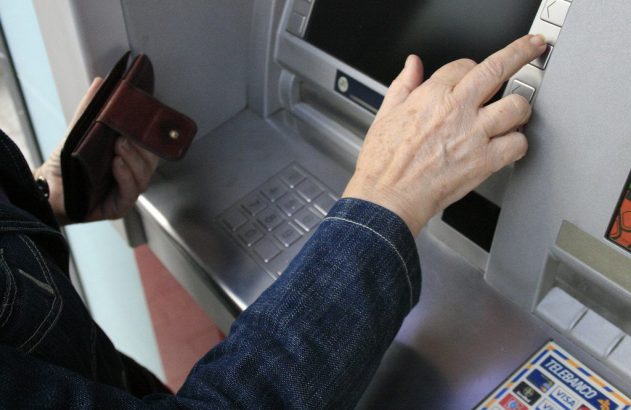 Pessoa usando caixa eletrônico, digitando e segurando carteira.