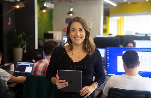 Mulher sorrindo, de pé, segurando tablet em escritório.