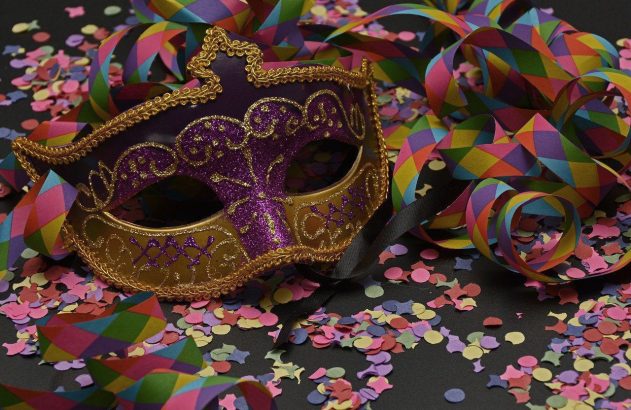 Máscara de carnaval roxa e dourada com confetes coloridos e serpentinas em fundo escuro.