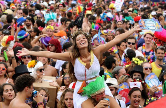 Mulher sorridente de braços abertos nos ombros de um homem em multidão celebrando o carnaval.