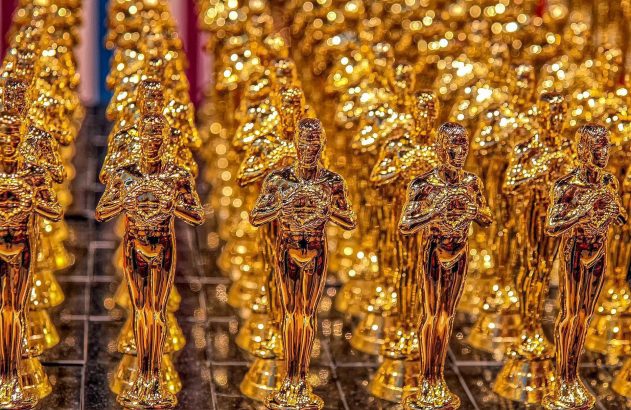 Fileiras de estatuetas douradas do Oscar reluzem com luzes desfocadas ao fundo.