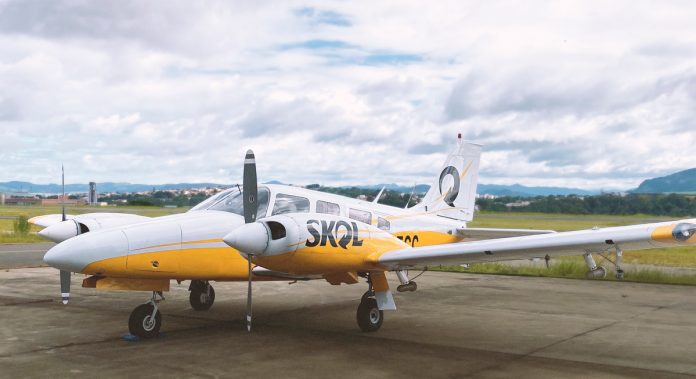 Avião bimotor branco e amarelo com a inscrição 'SACI', estacionado em pátio.