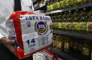 Pessoa em supermercado segura cesta básica embalada com 14 itens.