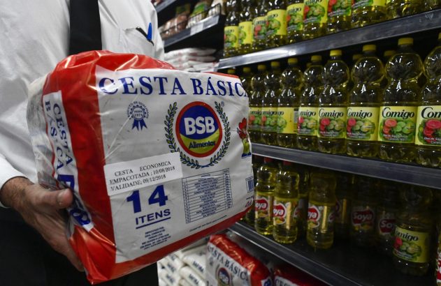 Pessoa em supermercado segura cesta básica embalada com 14 itens.