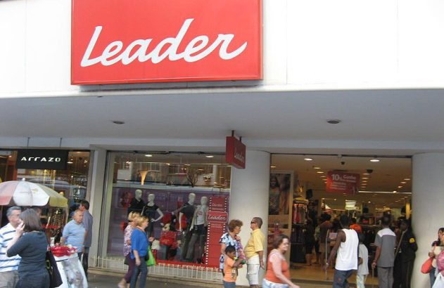 Entrada da loja Leader com movimento de pessoas. Letreiro vermelho 'Leader' visível.