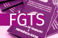 A imagem mostra algumas carteiras de trabalho empilhadas umas sobre as outras. Há uma faixa roxa sobre a foto, com a sigla FGTS escrita em branco.