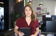 Mulher em pé no escritório segurando tablet e olhando para a câmera.