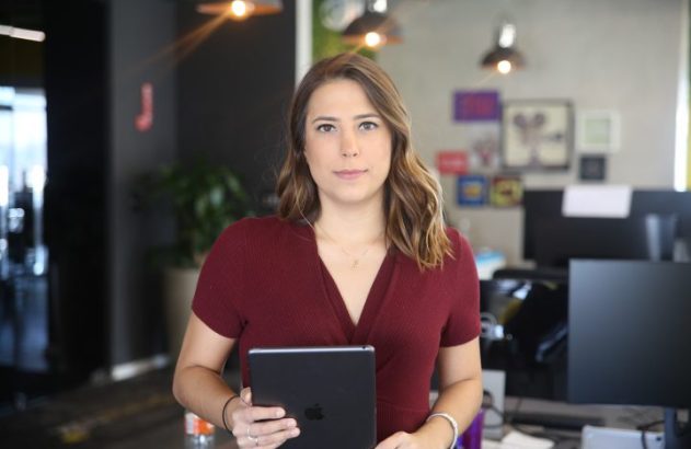 Mulher em pé no escritório segurando tablet e olhando para a câmera.