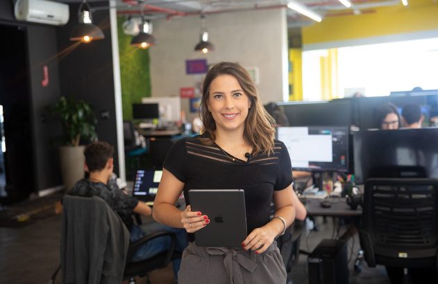 Mulher sorrindo, segurando um tablet, em um escritório.