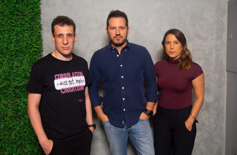 Três pessoas, dois homens e uma mulher, em pé, olhando para a câmera.