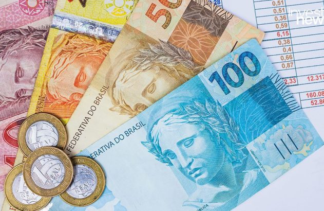 Cédulas e moedas de Real do Brasil sobre extratos financeiros com o logo 'invest news'.