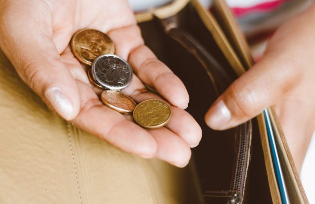 Mãos segurando moedas brasileiras sobre uma carteira aberta.