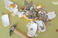 Cofrinho quebrado com moedas espalhadas e martelo ao lado.