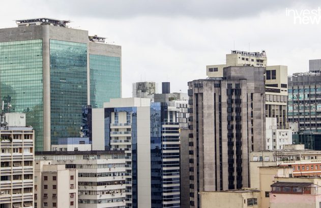 Paisagem urbana densa: múltiplos prédios de estilos variados, de vidro a concreto, sob céu cinza.