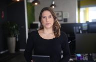 Mulher em escritório, segurando tablet, olhando para câmera.