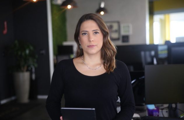 Mulher em escritório, segurando tablet, olhando para câmera.