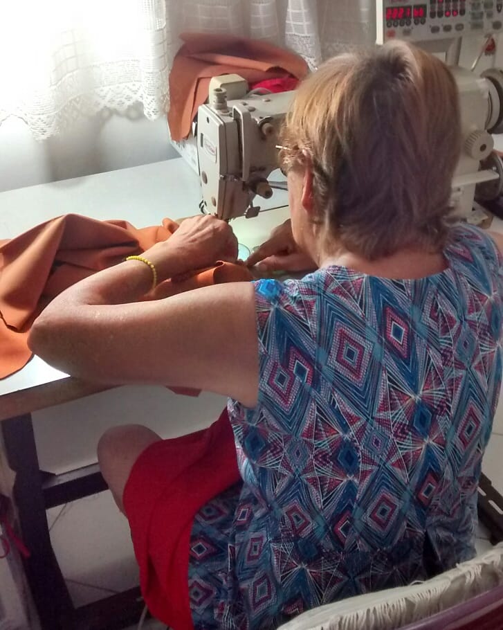 Mulher de costas costurando tecido em uma máquina de costura.