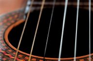 Detalhe de violão: boca escura, seis cordas e roseta decorativa.
