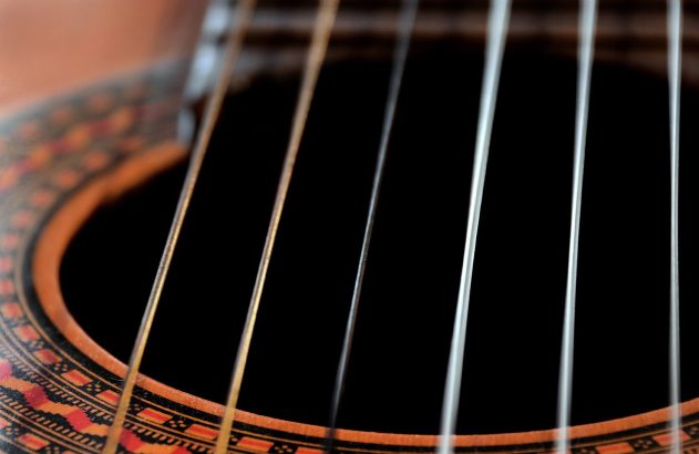 Detalhe de violão: boca escura, seis cordas e roseta decorativa.