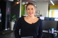 Mulher em camisa preta sorri para a câmera em um escritório.