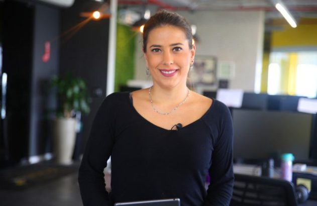 Mulher em camisa preta sorri para a câmera em um escritório.