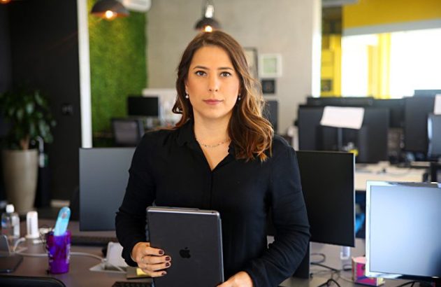 Mulher de preto em escritório moderno, segura tablet e olha para frente.