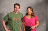 Homem e mulher sorrindo para a câmera, em frente a uma parede cinza.