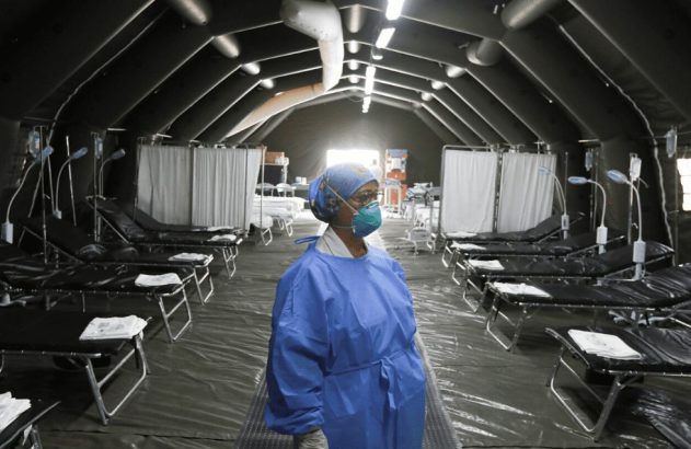 Profissional de saúde com máscara em tenda de hospital de campanha com leitos vazios.