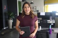 Mulher sorridente em pé, segurando um tablet, em um escritório.