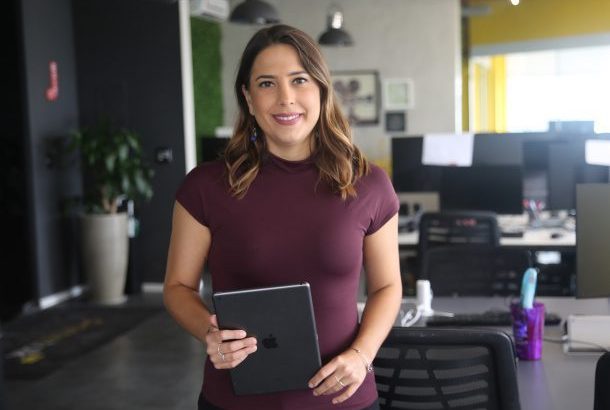 Mulher sorridente em pé, segurando um tablet, em um escritório.