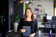 Mulher profissional em escritório, segurando tablet e olhando para frente.